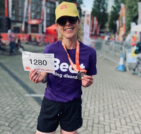 Woman holding a medal and certificate wearing a purple Beat t-shirt, sunglasses and a yellow hat